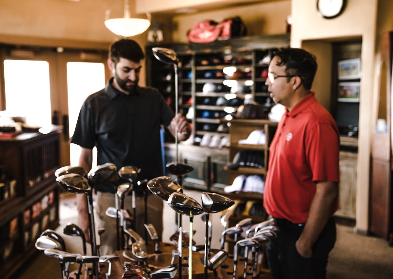 Two men browsing golf clubs in a sports equipment store, discussing options.